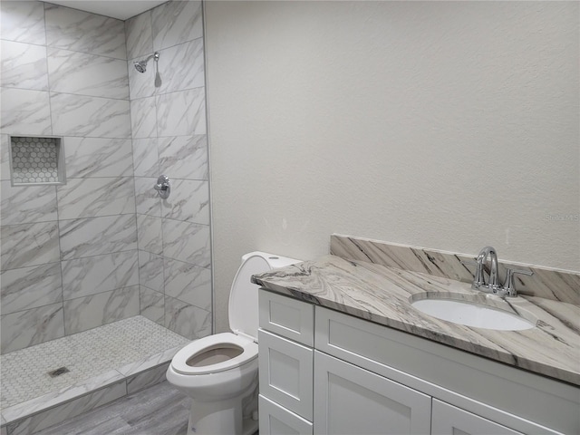 bathroom with hardwood / wood-style floors, toilet, vanity, and a tile shower