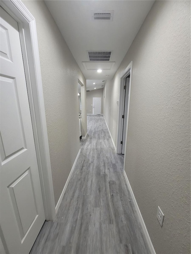 hall with wood finished floors, visible vents, a textured wall, and baseboards