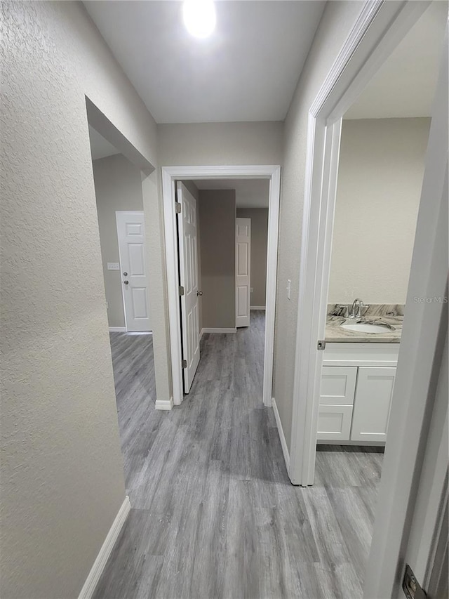 hall featuring a sink, baseboards, light wood-style flooring, and a textured wall