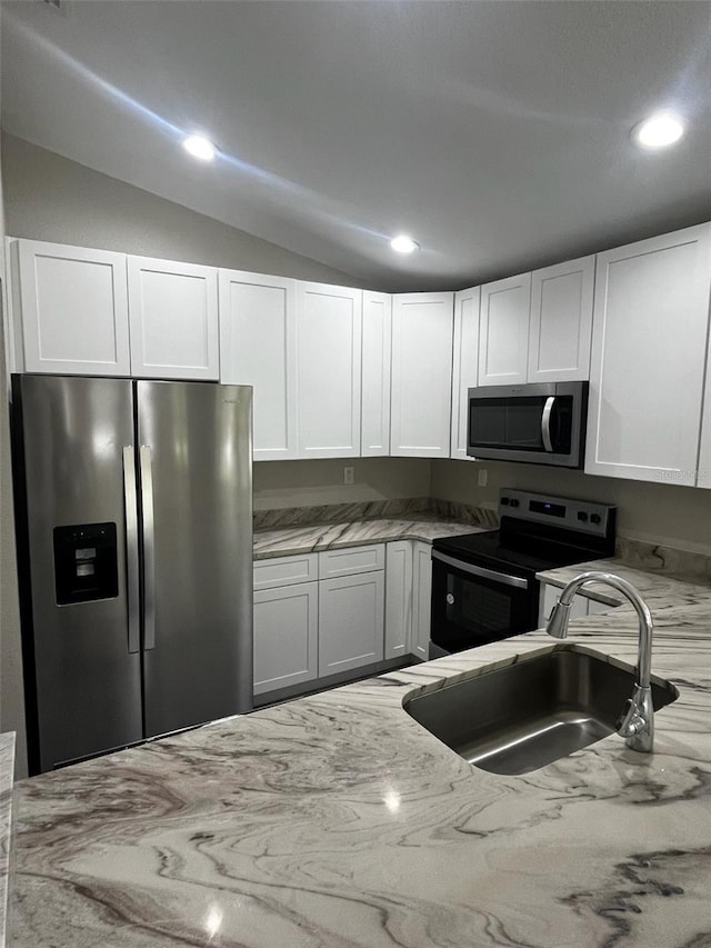 kitchen with light stone counters, vaulted ceiling, appliances with stainless steel finishes, and a sink