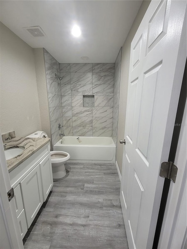 bathroom featuring vanity, wood finished floors, visible vents, tub / shower combination, and toilet