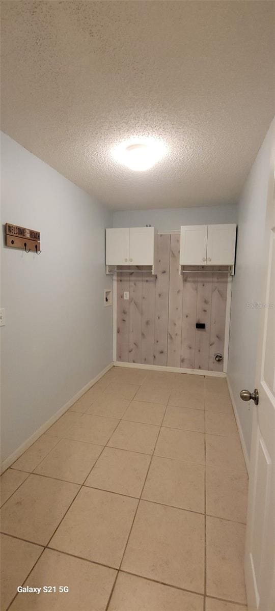 laundry room with light tile patterned flooring, cabinets, and a textured ceiling