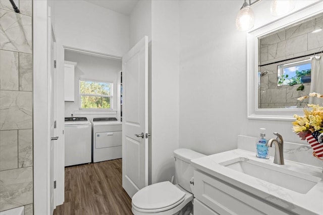 bathroom featuring a tile shower, vanity, hardwood / wood-style floors, washing machine and clothes dryer, and toilet