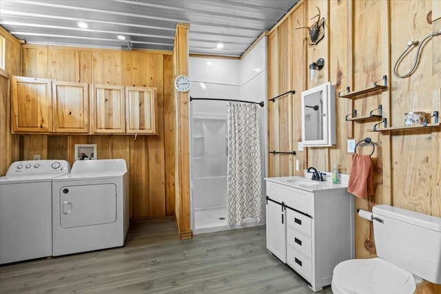 laundry room featuring light hardwood / wood-style flooring, wooden walls, sink, and washing machine and clothes dryer