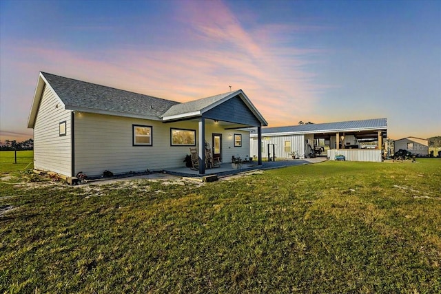 back house at dusk featuring a patio area and a lawn