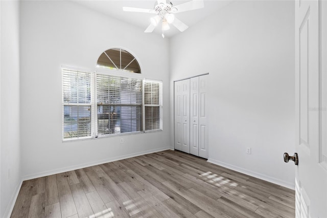 empty room with ceiling fan, baseboards, a high ceiling, and wood finished floors