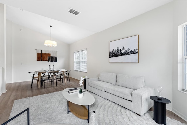 living room with visible vents, wood finished floors, baseboards, and vaulted ceiling