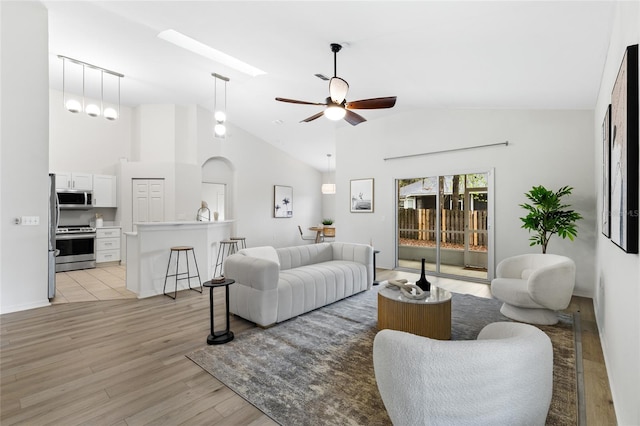 living area with a skylight, high vaulted ceiling, light wood-style floors, and a ceiling fan