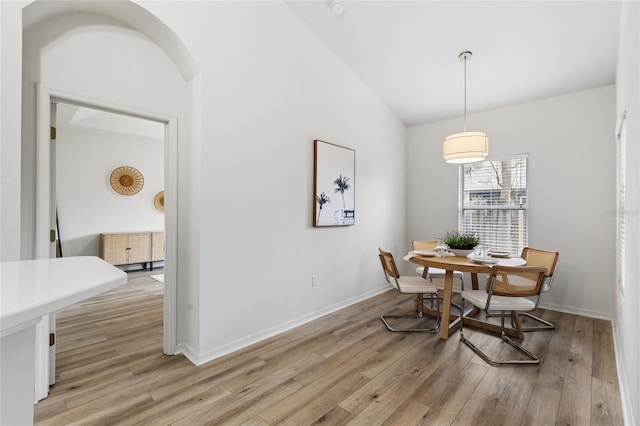 dining space with baseboards, light wood-type flooring, arched walkways, and lofted ceiling