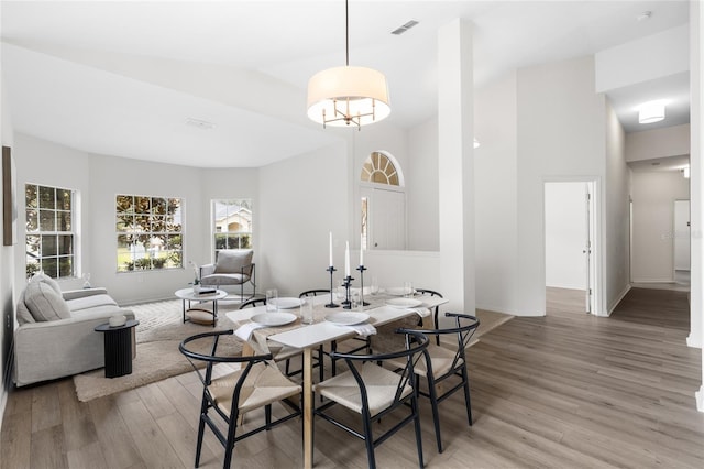 dining space featuring visible vents, lofted ceiling, light wood-style floors, and baseboards