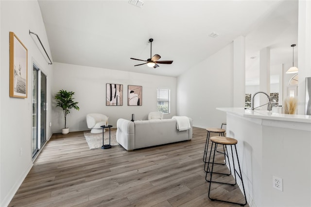 living room with visible vents, ceiling fan, baseboards, vaulted ceiling, and wood finished floors