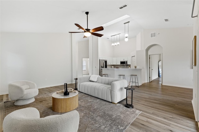 living room with visible vents, high vaulted ceiling, a ceiling fan, arched walkways, and light wood finished floors