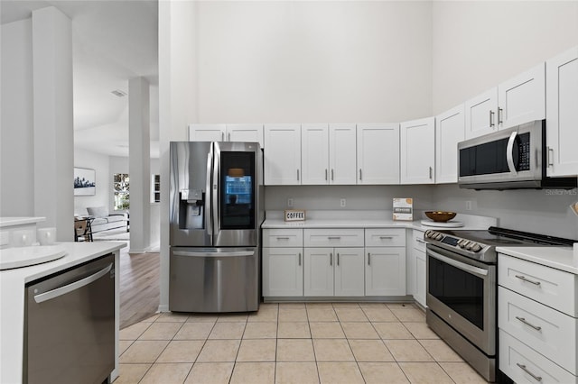 kitchen with stainless steel appliances, a towering ceiling, light tile patterned flooring, and light countertops