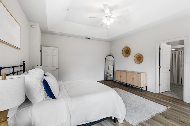 bedroom featuring ceiling fan, a tray ceiling, visible vents, and wood finished floors