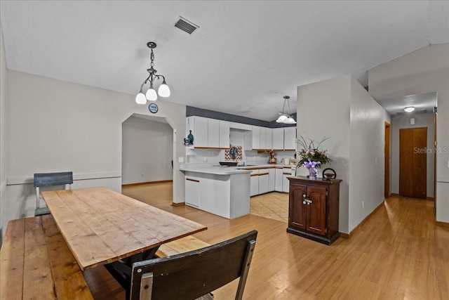 kitchen featuring light hardwood / wood-style floors, white cabinetry, an inviting chandelier, pendant lighting, and vaulted ceiling