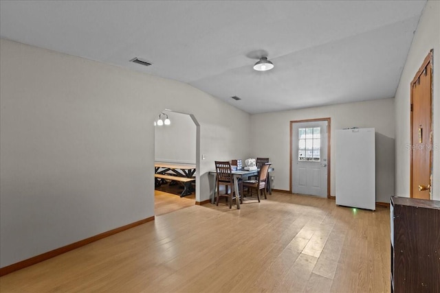 dining space with arched walkways, vaulted ceiling, baseboards, and light wood-style floors