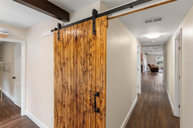 corridor with beam ceiling, a barn door, and dark wood-type flooring