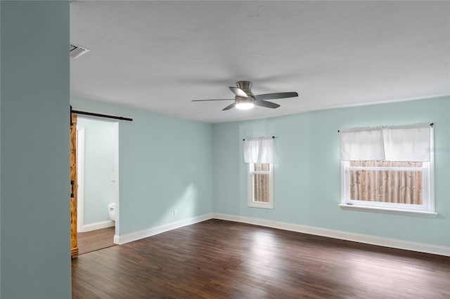 empty room with dark hardwood / wood-style flooring, a barn door, and ceiling fan