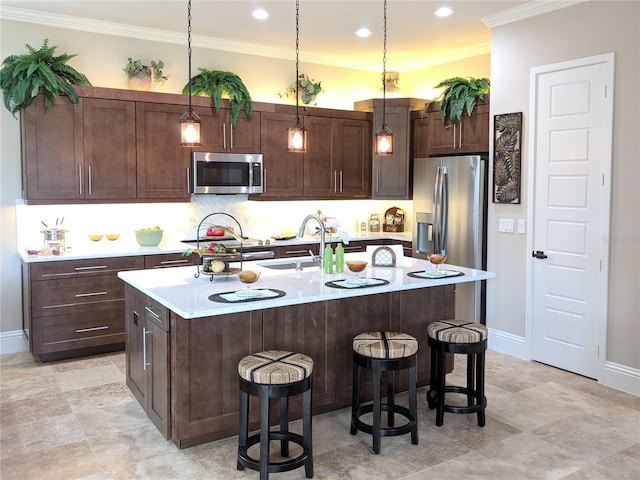 kitchen featuring appliances with stainless steel finishes, decorative light fixtures, dark brown cabinets, sink, and a kitchen island with sink