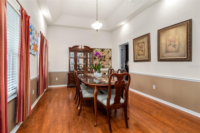 dining room with dark wood-type flooring and a tray ceiling