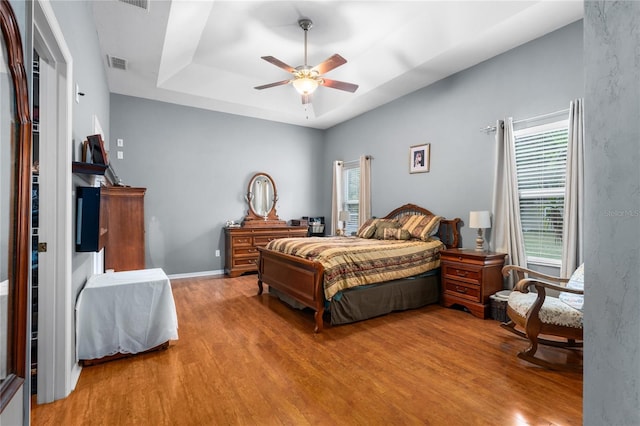 bedroom featuring wood finished floors, a tray ceiling, a ceiling fan, and baseboards