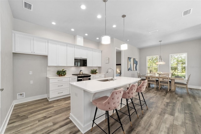 kitchen featuring stainless steel appliances, white cabinets, sink, an island with sink, and pendant lighting