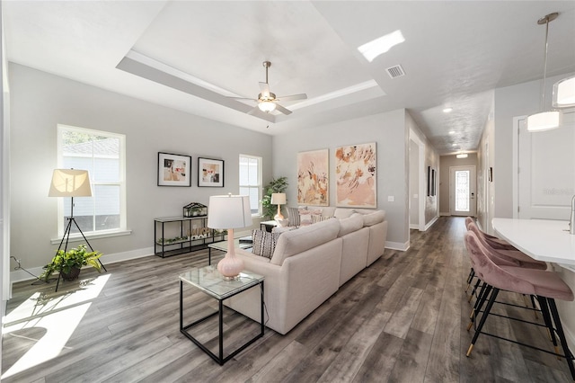 living room featuring dark hardwood / wood-style flooring, ceiling fan, and a tray ceiling