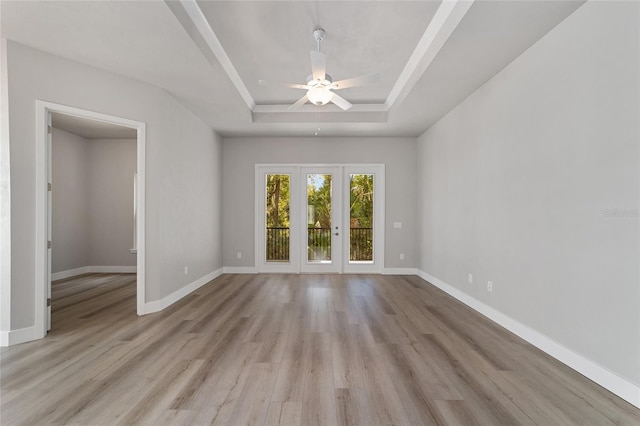 empty room with ceiling fan, a raised ceiling, light wood-type flooring, and french doors