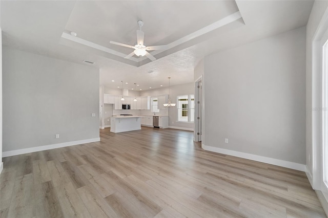 unfurnished living room with ceiling fan with notable chandelier, light wood-type flooring, and a tray ceiling