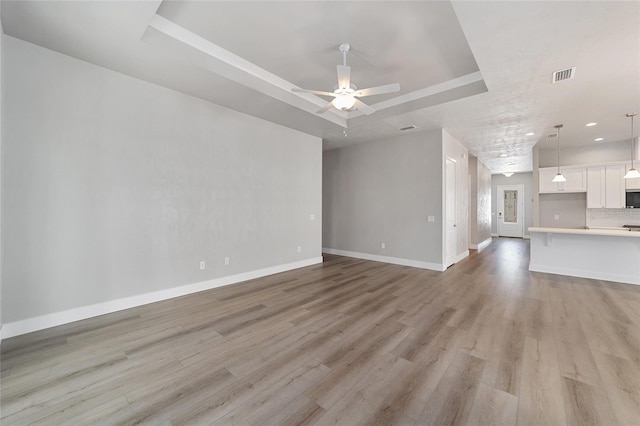 unfurnished living room with ceiling fan, light hardwood / wood-style floors, and a raised ceiling