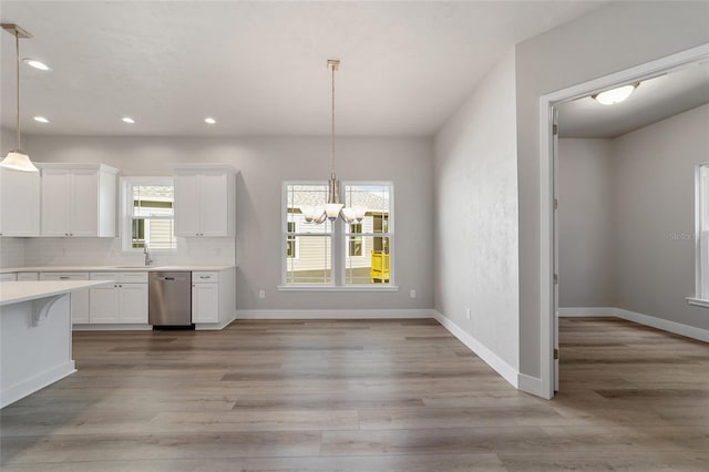 kitchen featuring white cabinets, light wood-type flooring, stainless steel dishwasher, and pendant lighting