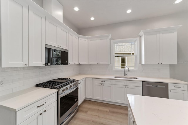 kitchen featuring stainless steel appliances, sink, backsplash, white cabinets, and light wood-type flooring