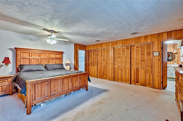 bedroom with visible vents, two closets, a textured ceiling, and carpet floors