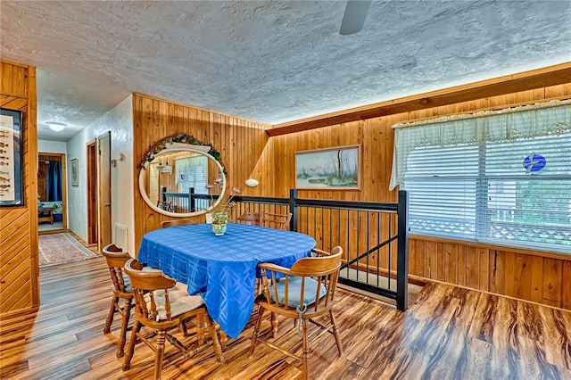 dining space with wooden walls, a textured ceiling, and wood finished floors