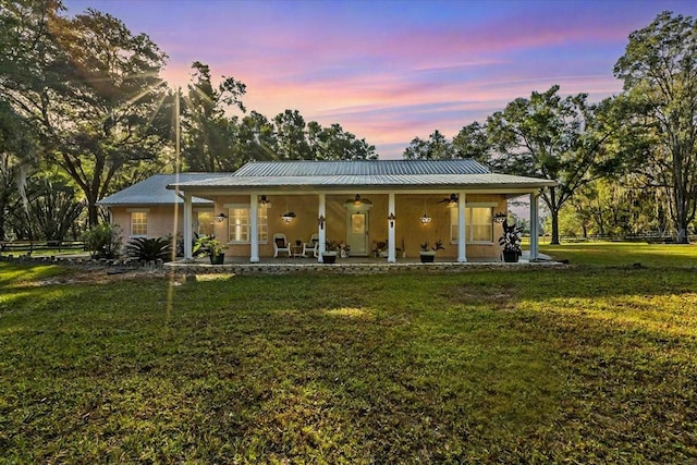 back house at dusk featuring a porch, ceiling fan, and a lawn