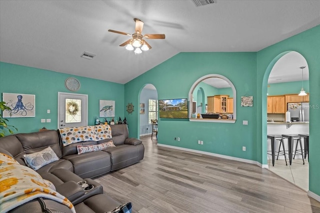 living room with a textured ceiling, ceiling fan, light hardwood / wood-style flooring, and lofted ceiling