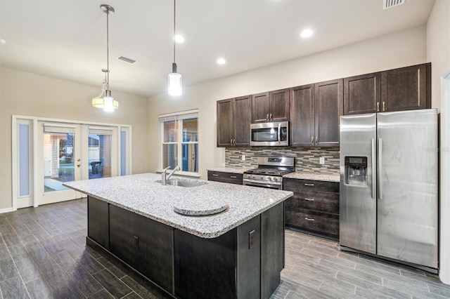 kitchen with french doors, hanging light fixtures, sink, a kitchen island with sink, and appliances with stainless steel finishes