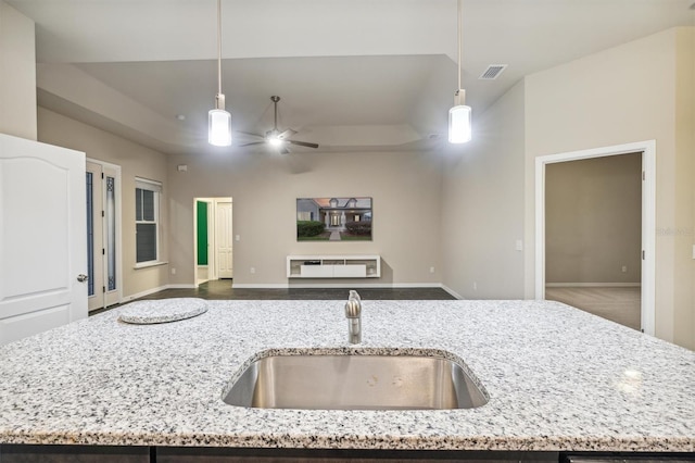 kitchen featuring an island with sink, sink, decorative light fixtures, and light stone counters