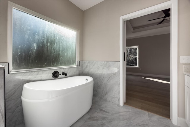 bathroom with a wealth of natural light, a bathtub, tile walls, and ceiling fan