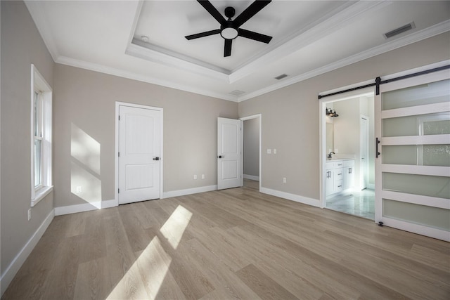 unfurnished bedroom with ceiling fan, crown molding, a barn door, connected bathroom, and light hardwood / wood-style floors