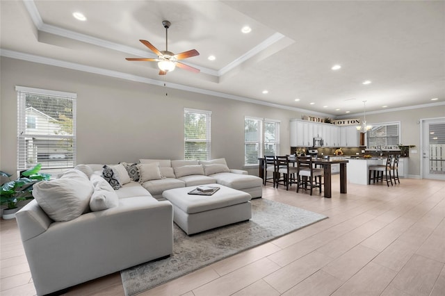 living room with a raised ceiling, ornamental molding, ceiling fan, and light wood-type flooring