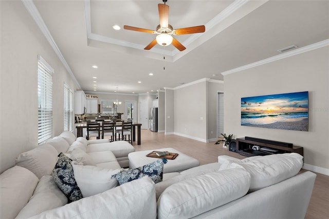 living room with a raised ceiling, crown molding, ceiling fan, and light hardwood / wood-style floors