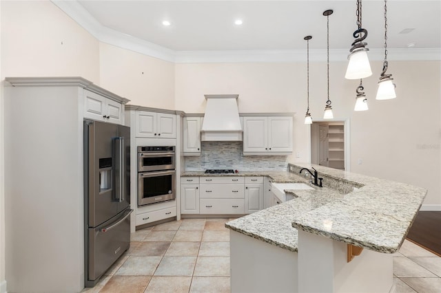 kitchen with stainless steel appliances, sink, light stone countertops, pendant lighting, and premium range hood