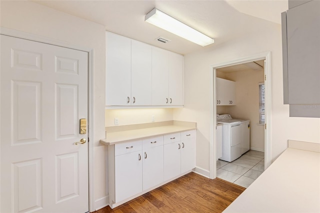 clothes washing area with cabinets, independent washer and dryer, and light hardwood / wood-style flooring