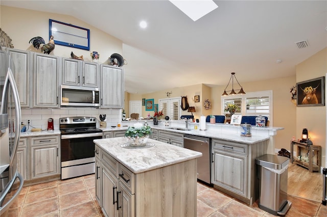 kitchen with stainless steel appliances, light stone counters, vaulted ceiling, kitchen peninsula, and a kitchen island