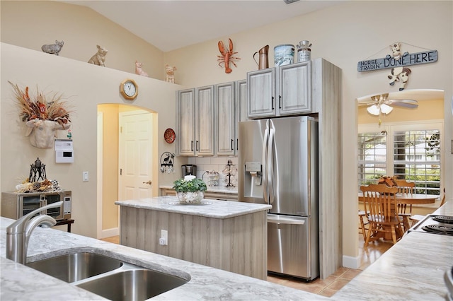 kitchen with sink, stainless steel refrigerator with ice dispenser, light tile patterned floors, a kitchen island, and vaulted ceiling