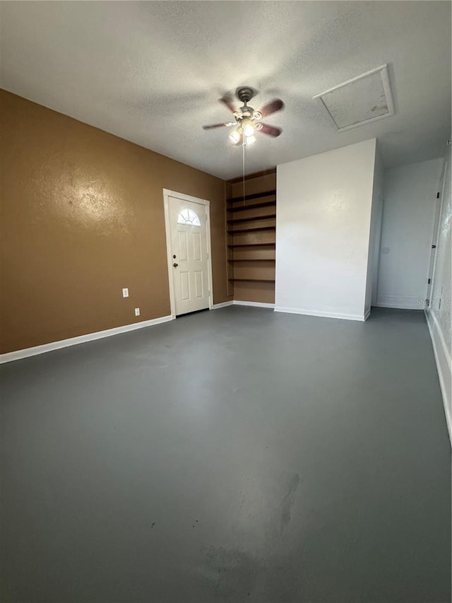 unfurnished room featuring baseboards, ceiling fan, finished concrete floors, a textured ceiling, and attic access