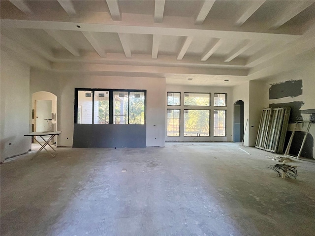 unfurnished living room featuring beam ceiling, a towering ceiling, and concrete floors