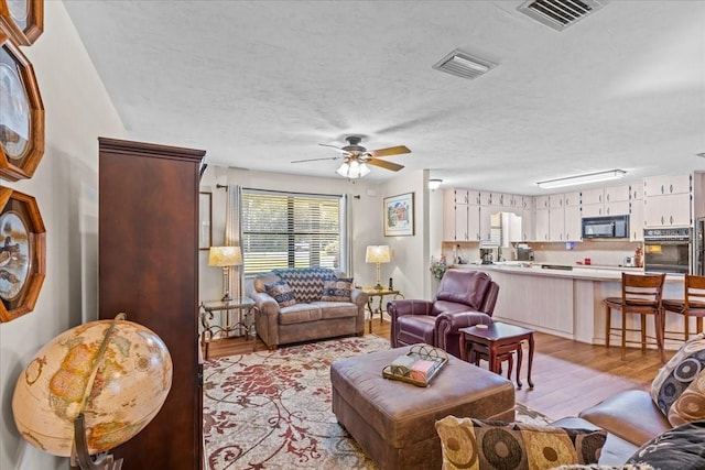 living room with light hardwood / wood-style floors, a textured ceiling, and ceiling fan