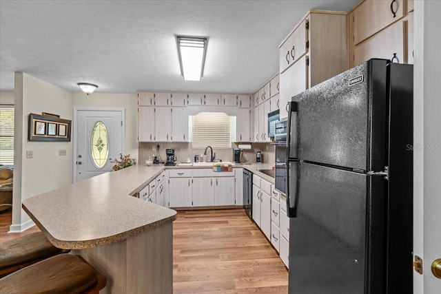 kitchen featuring black appliances, kitchen peninsula, tasteful backsplash, a kitchen bar, and light wood-type flooring